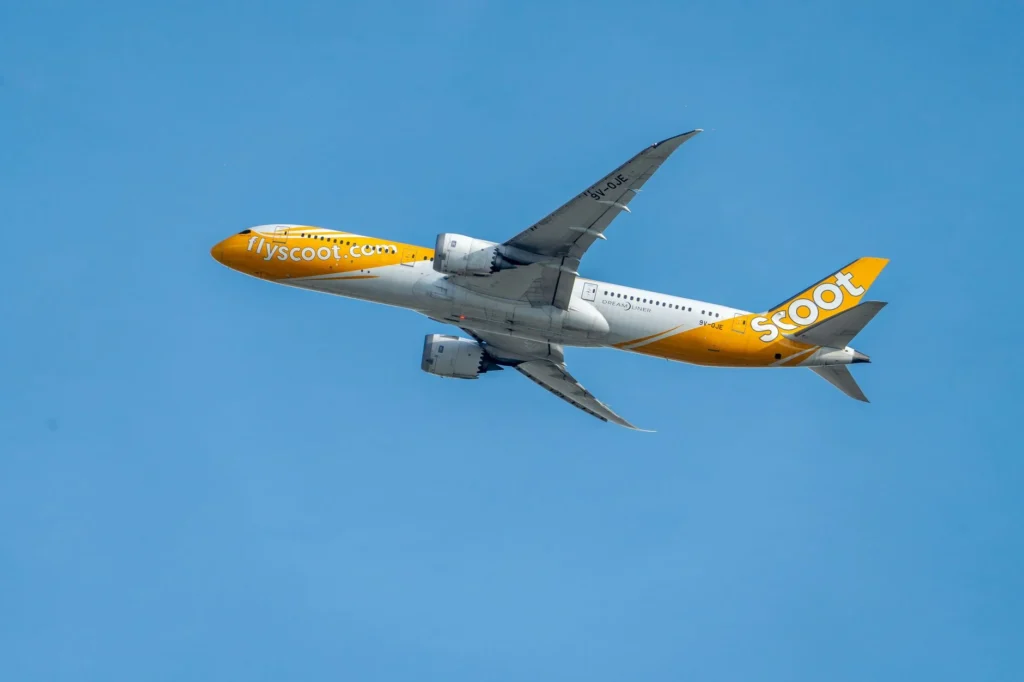 Scoot airline's Boeing 787 Dreamliner soaring through a clear blue sky. Captured in daytime, showcasing the aircraft's design and livery.