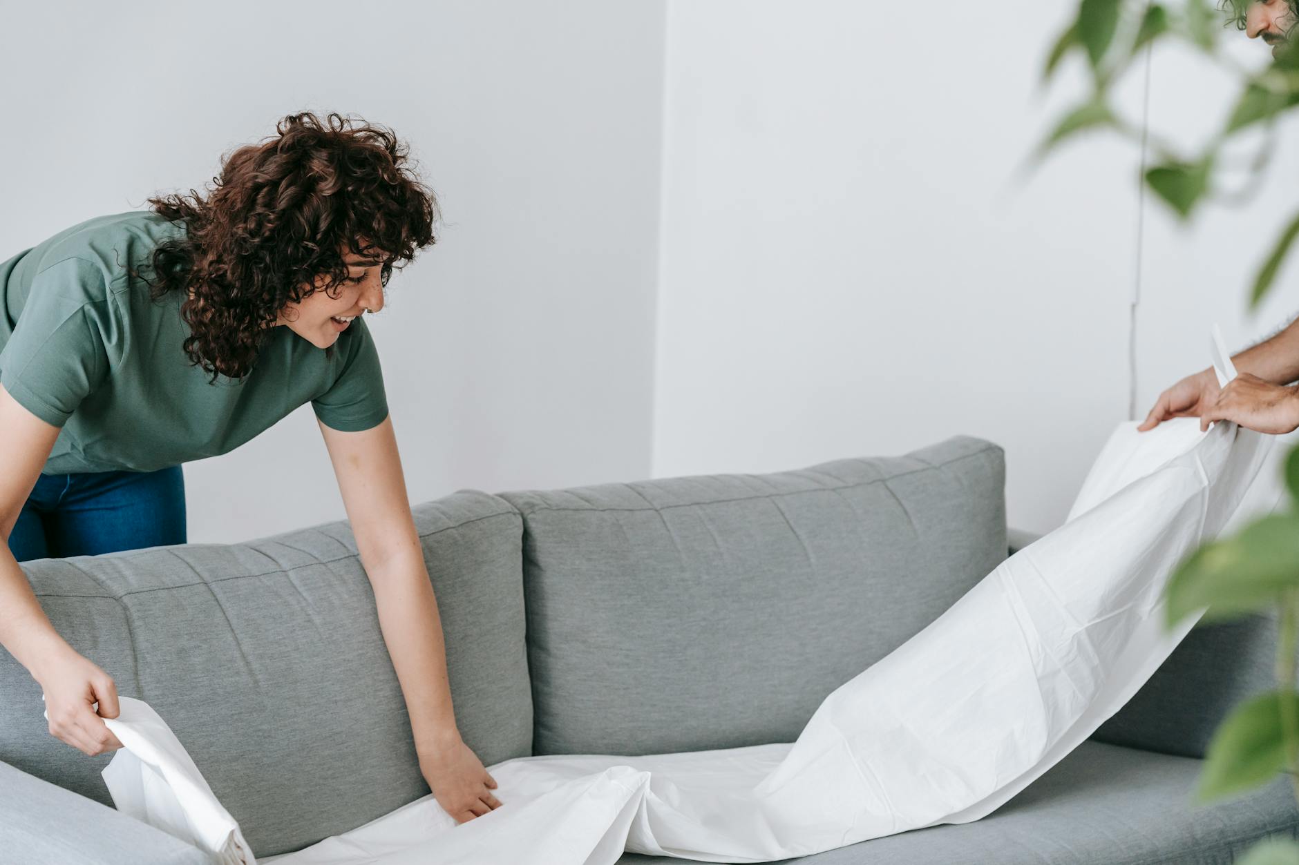 A happy couple adjusting a white cover on a grey sofa together in a cozy home setting.