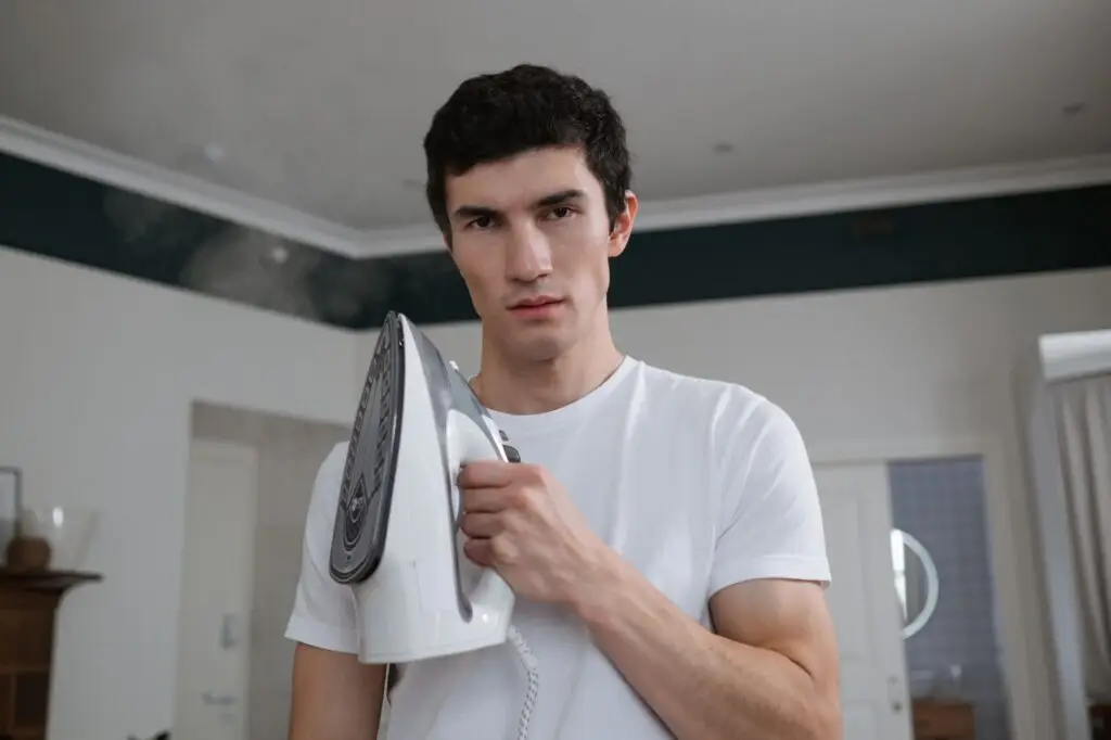 Young adult man holding a steam iron in a contemporary living room, preparing for housework.