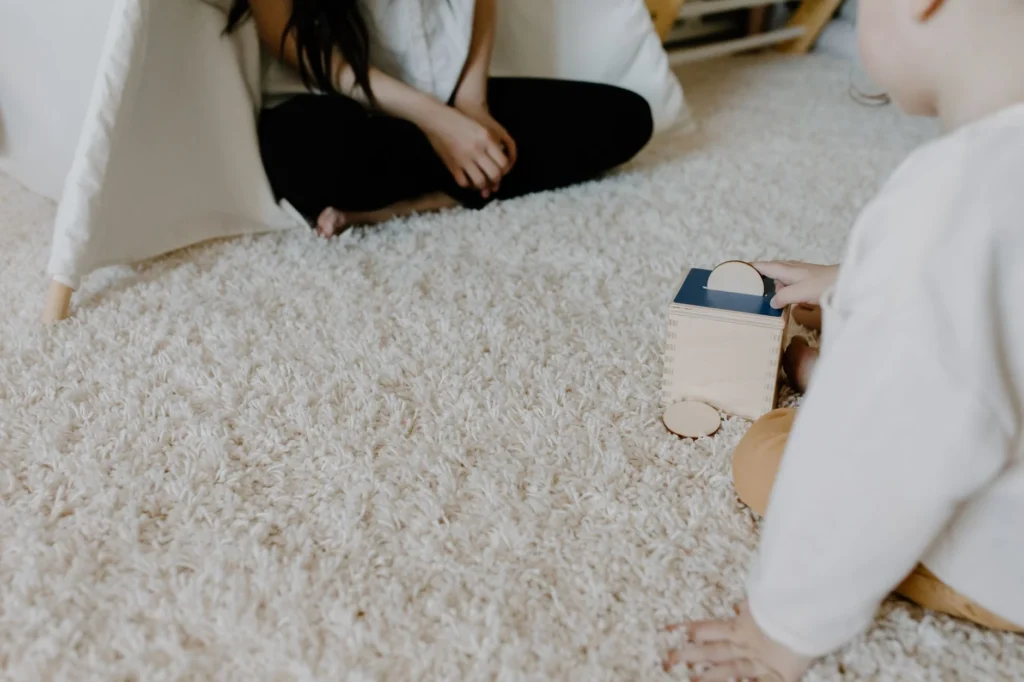 A child plays with a wooden block toy on a cozy carpet indoors, creating a warm family moment.