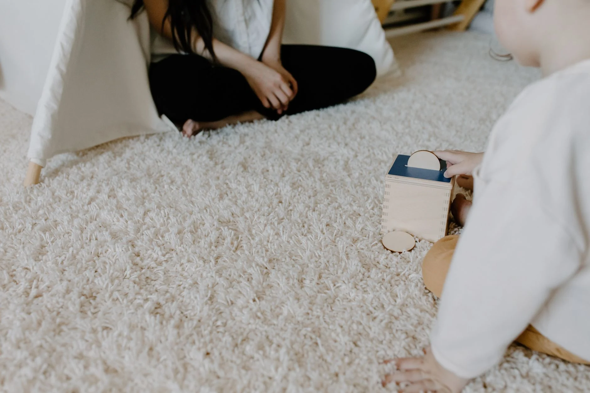 A child plays with a wooden block toy on a cozy carpet indoors, creating a warm family moment.