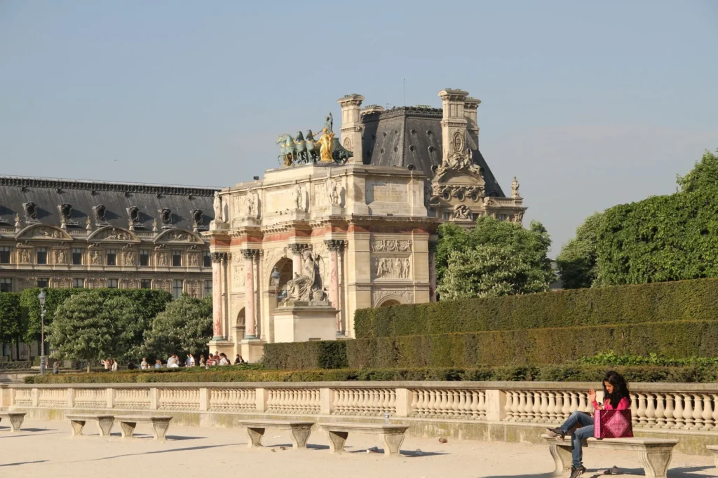 Sunny day at the Arc de Triomphe du Carrousel in Paris with people relaxing nearby.