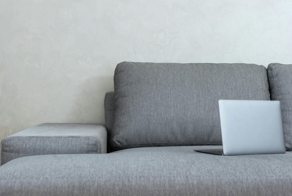 Interior of light modern apartment with open netbook placed on couch with pillows near wall