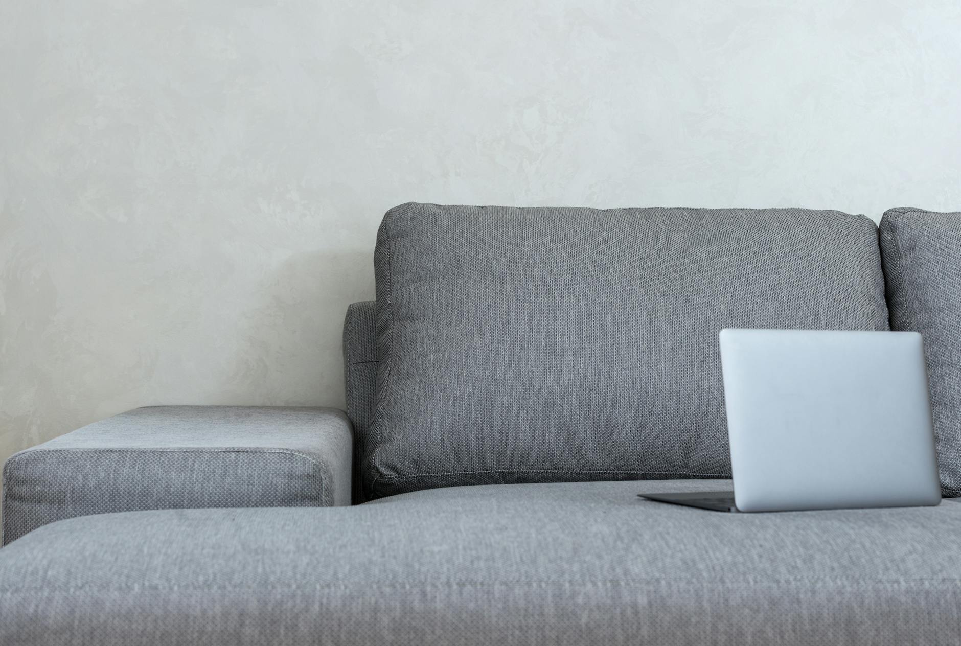 Interior of light modern apartment with open netbook placed on couch with pillows near wall