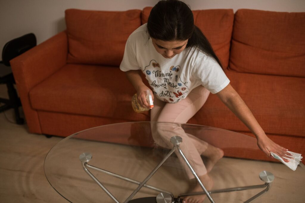 Adult woman wiping a glass table with spray in a cozy living room setting.