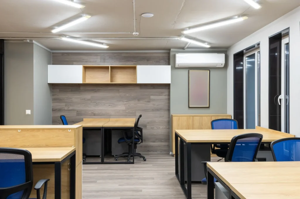 New wooden desks and blue chairs placed in spacious contemporary workplace illuminated by lamps