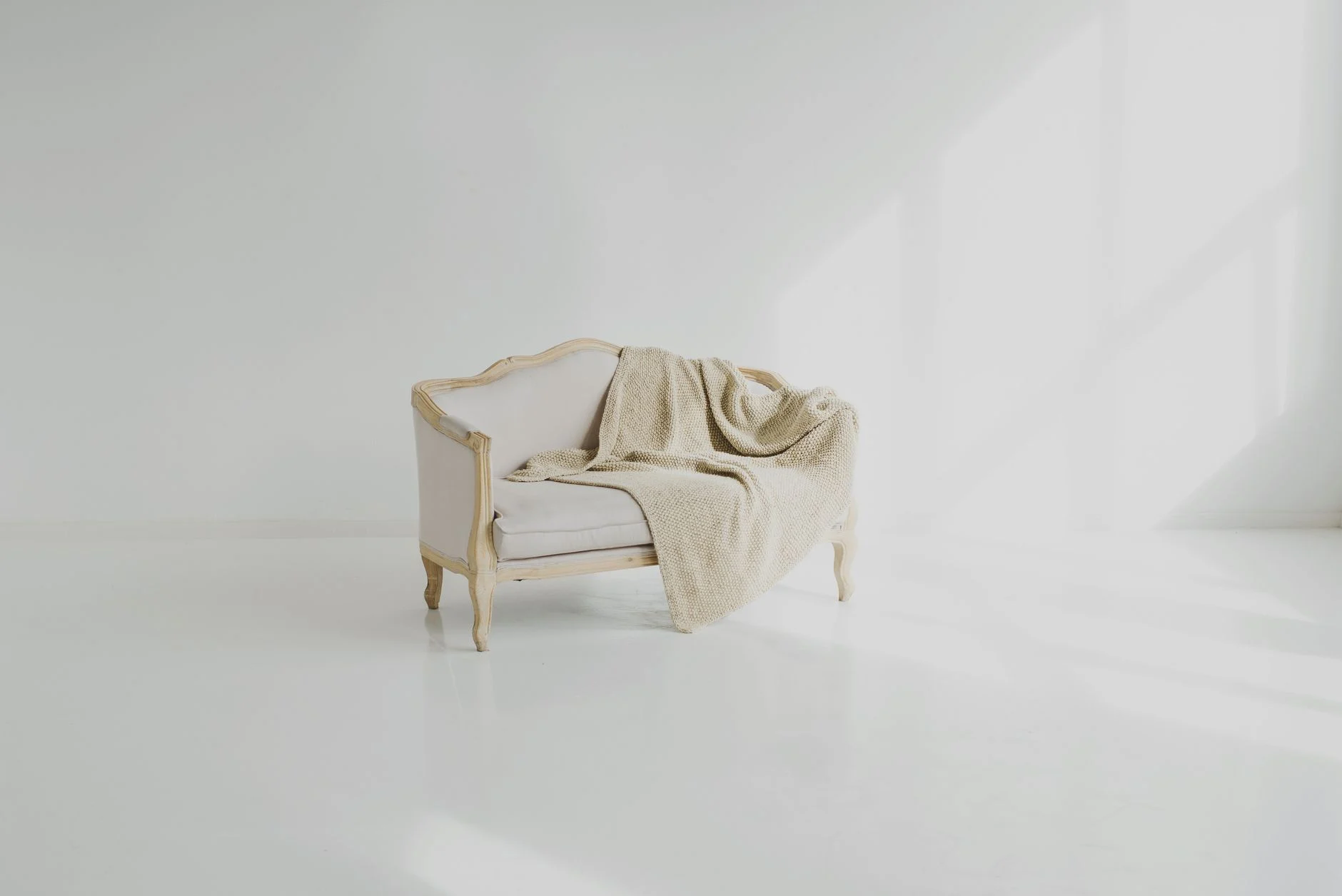 A beige throw on a vintage white sofa in a bright minimalist living space.