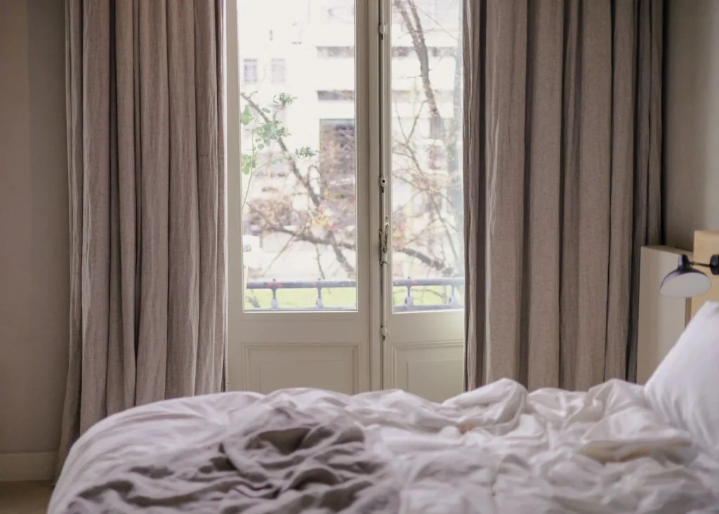 Peaceful bedroom with unmade bed and view through curtains.