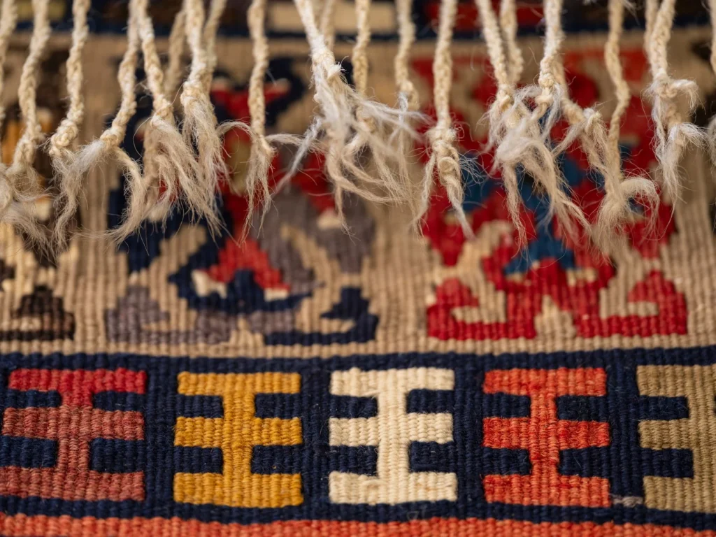 Detailed close-up of a colorful woven textile with fringes, showcasing intricate patterns and textures.