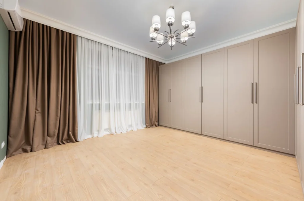 Modern closet on wooden floor under lamp and air conditioning in empty house room with curtains