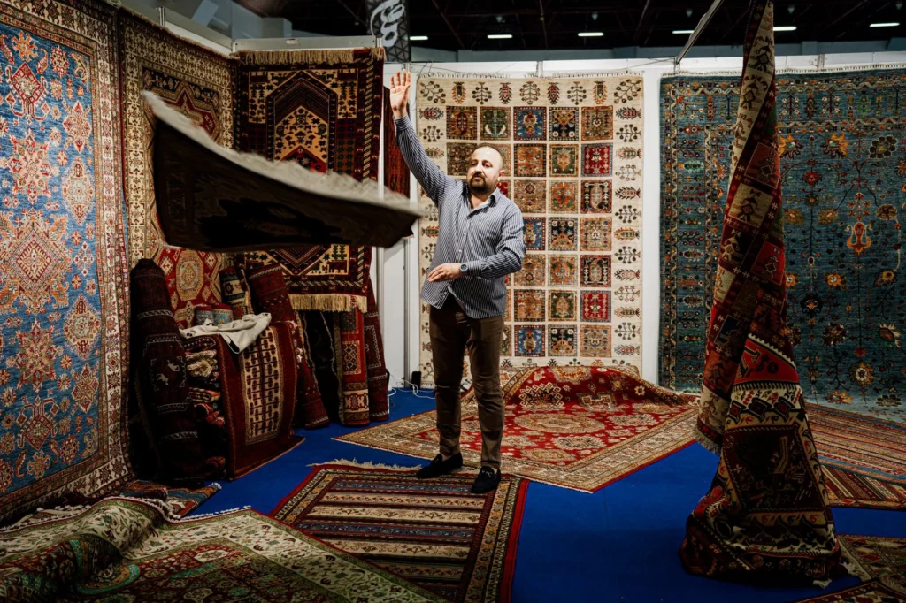 A man showcases traditional Persian rugs at an indoor market stall.