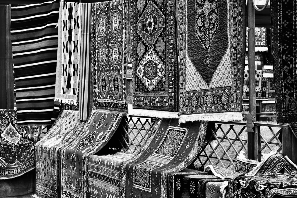 A black and white photo of hanging traditional rugs in a market bazaar.