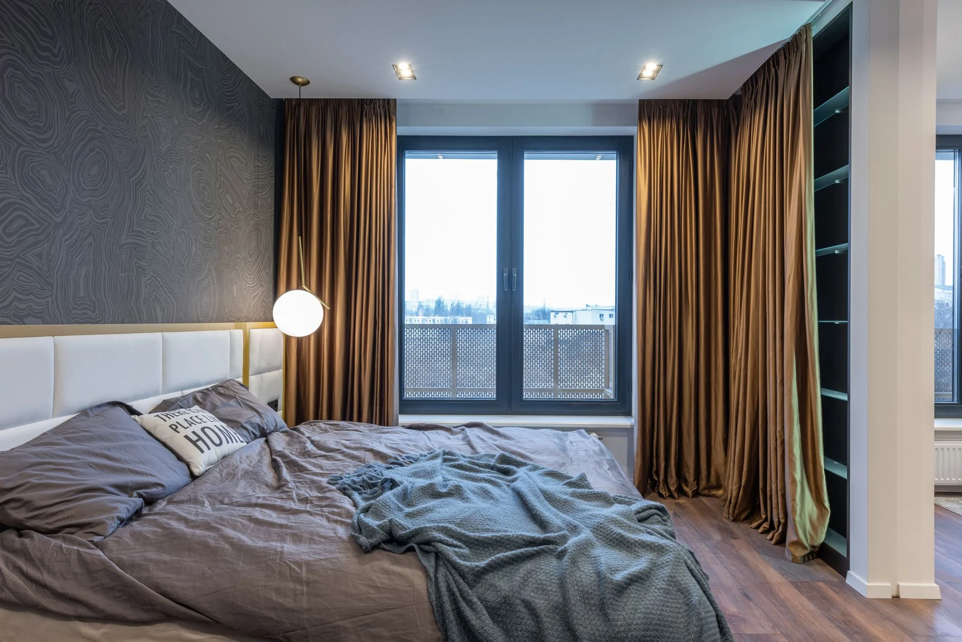 Interior of light modern flat with soft bed with pillows and blanket near lamp and window with curtains