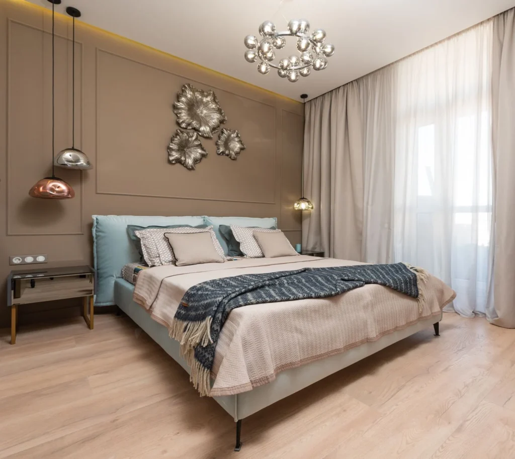 Interior of hotel room with bed next to table under lamps hanging from ceiling near window with curtains
