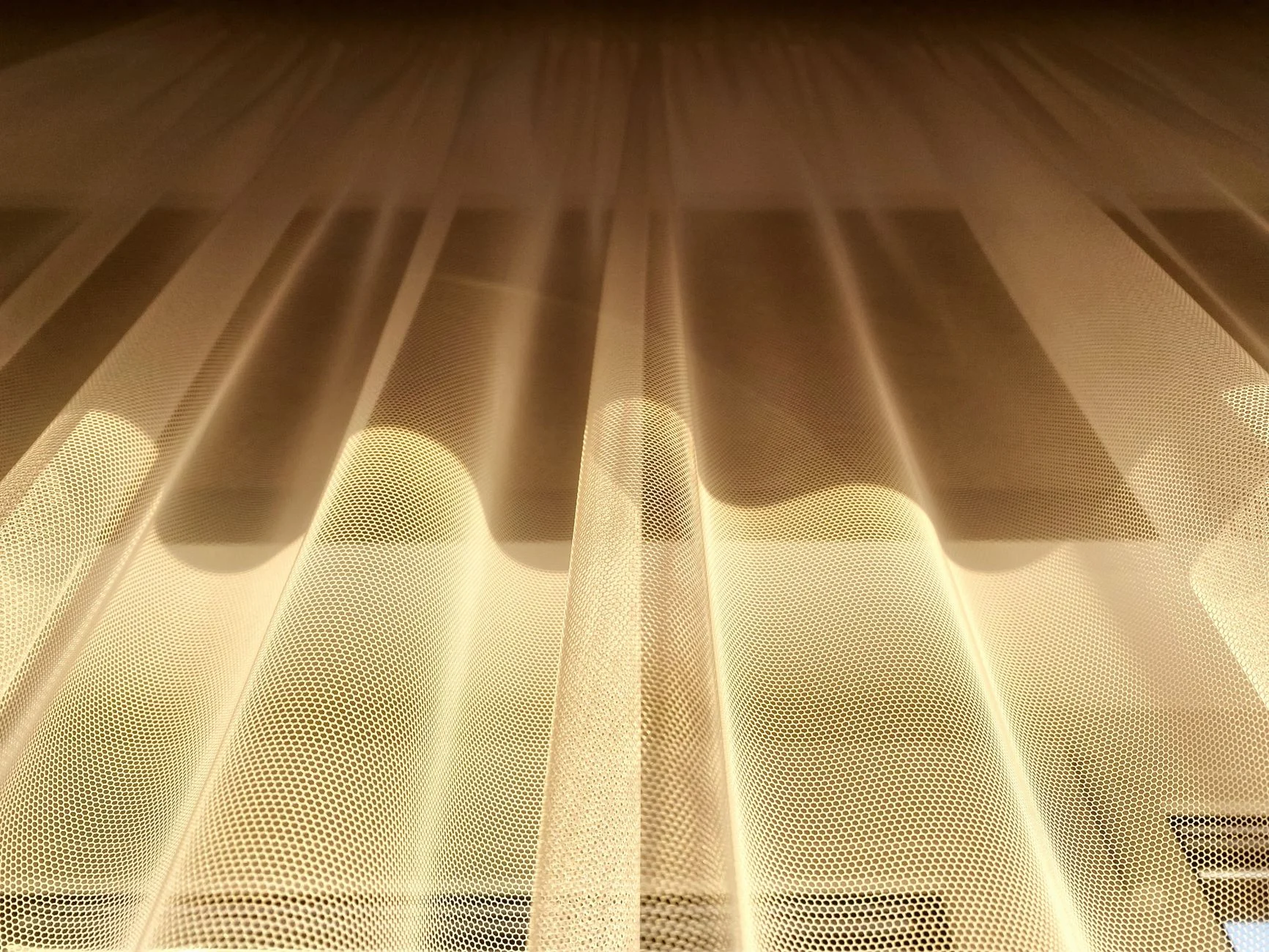 A low-angle shot of golden sheer curtains beautifully illuminated by sunlight.