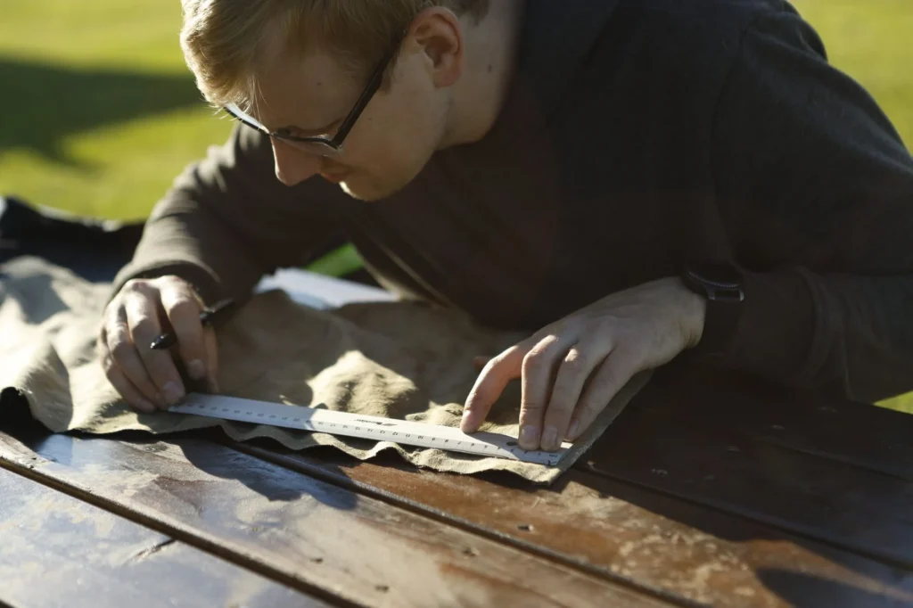 A focused man measuring fabric with a ruler outdoors in Estonia, highlighting precision in craftwork.