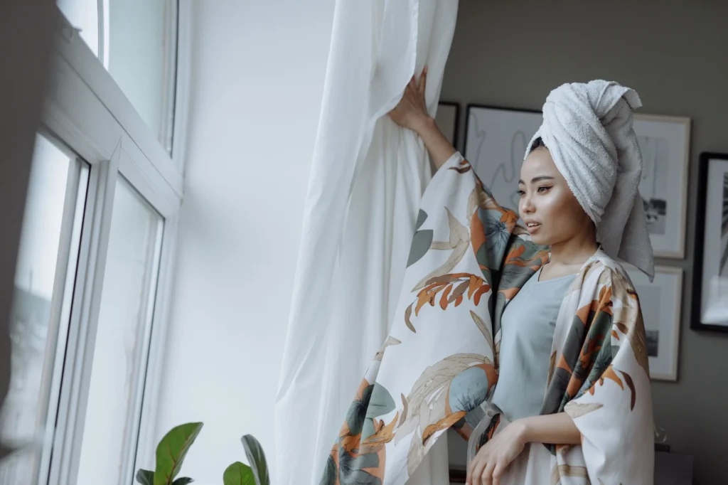 Young woman in floral kimono enjoying a bright morning indoors by the window.