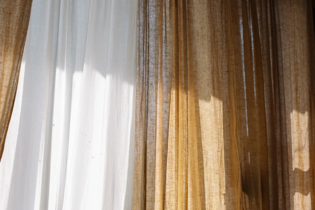 Warm sunlight streams through textured curtains, creating a calm indoor ambiance.
