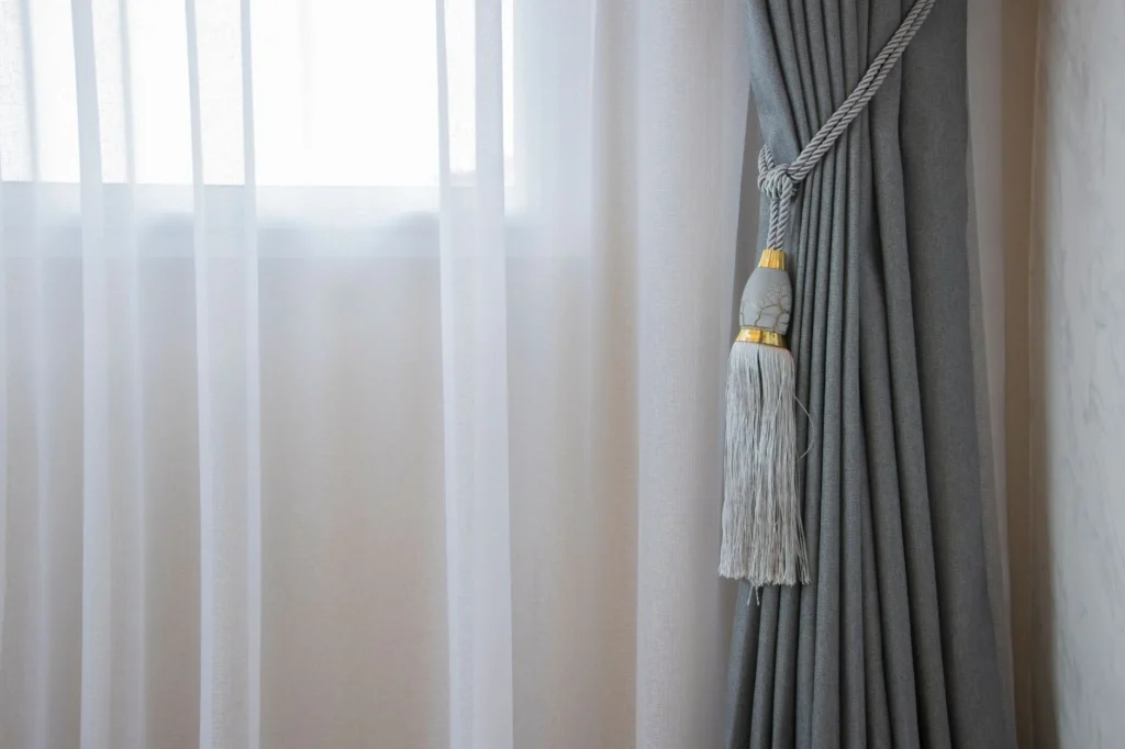 Soft gray curtain with decorative tieback in a bright room, adding elegance to home decor.