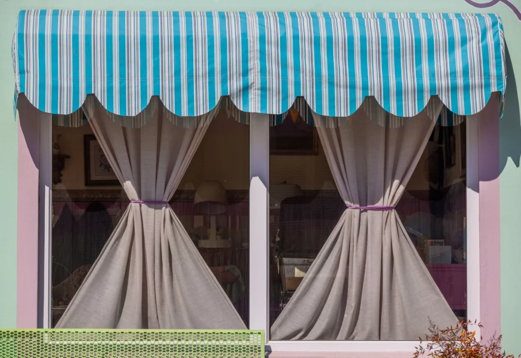 A colorful window with a blue striped awning and tied-back curtains, offering a cozy and inviting look.