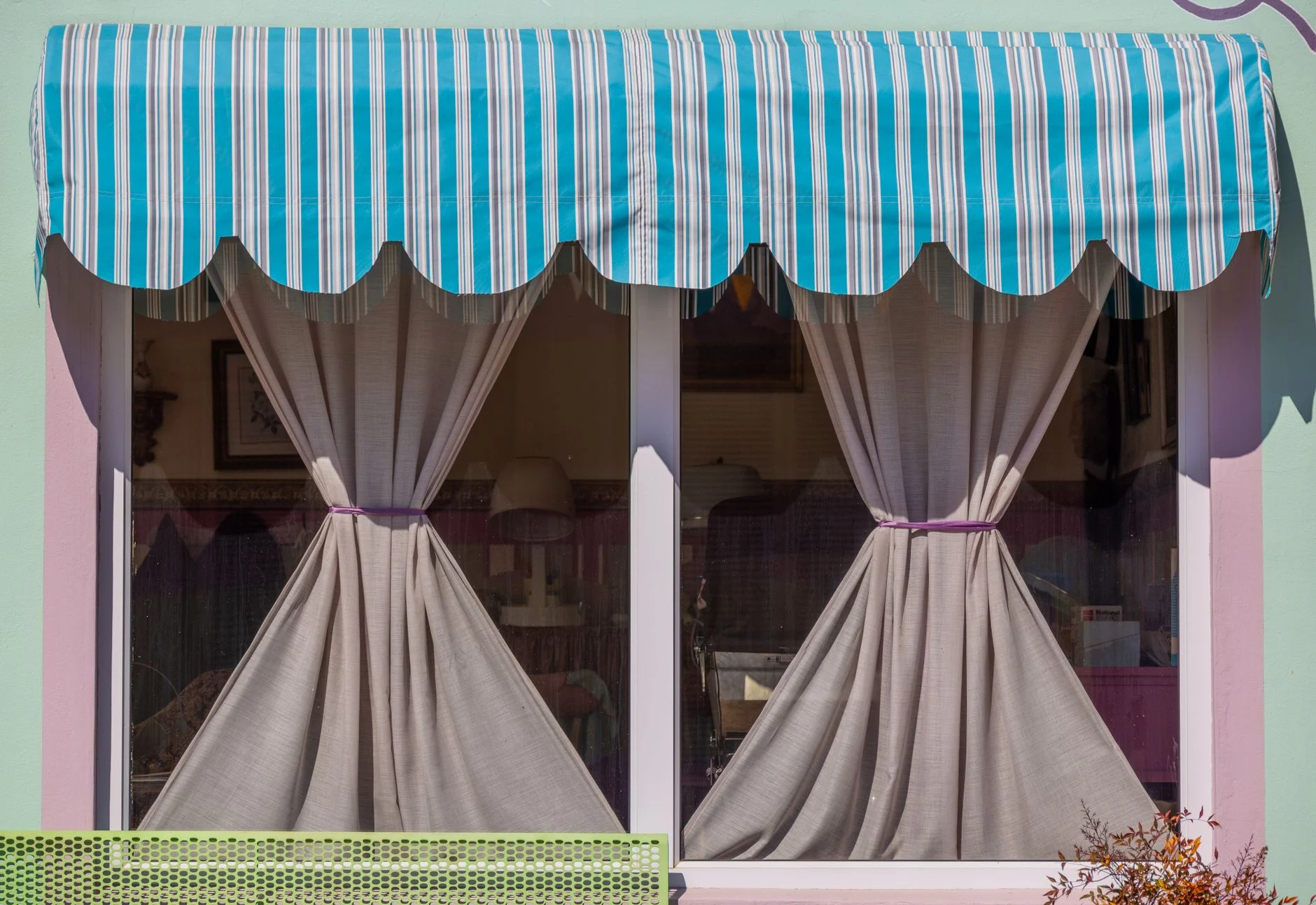A colorful window with a blue striped awning and tied-back curtains, offering a cozy and inviting look.
