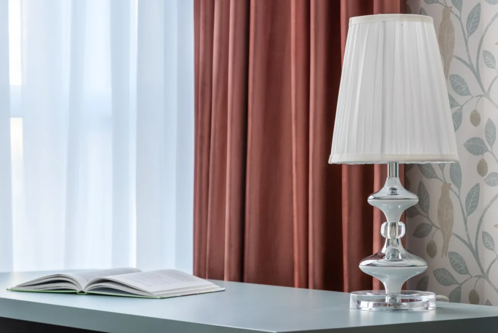 Decorative lamp and open textbook on smooth table against curtains and wall with bird ornament in light house