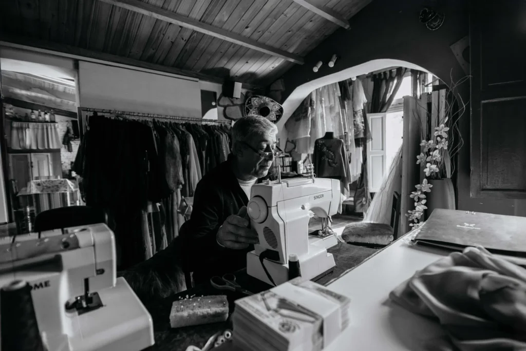 Black and white photo of a tailor focused on sewing in a vintage workshop.