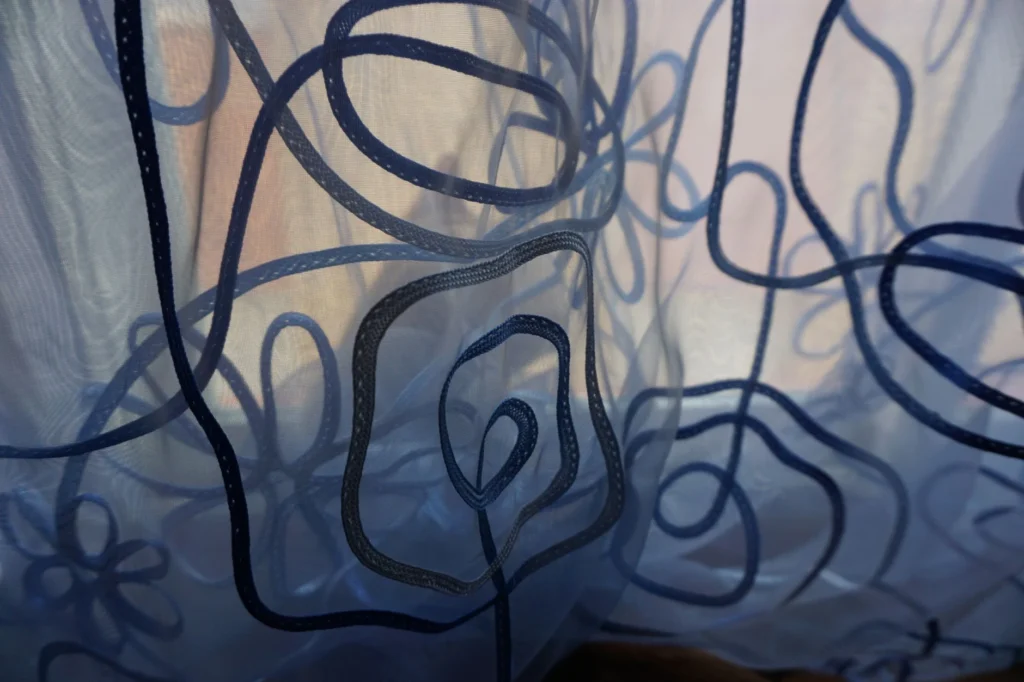 Delicate fabric curtains showcase intricate designs, softly illuminated by natural light.