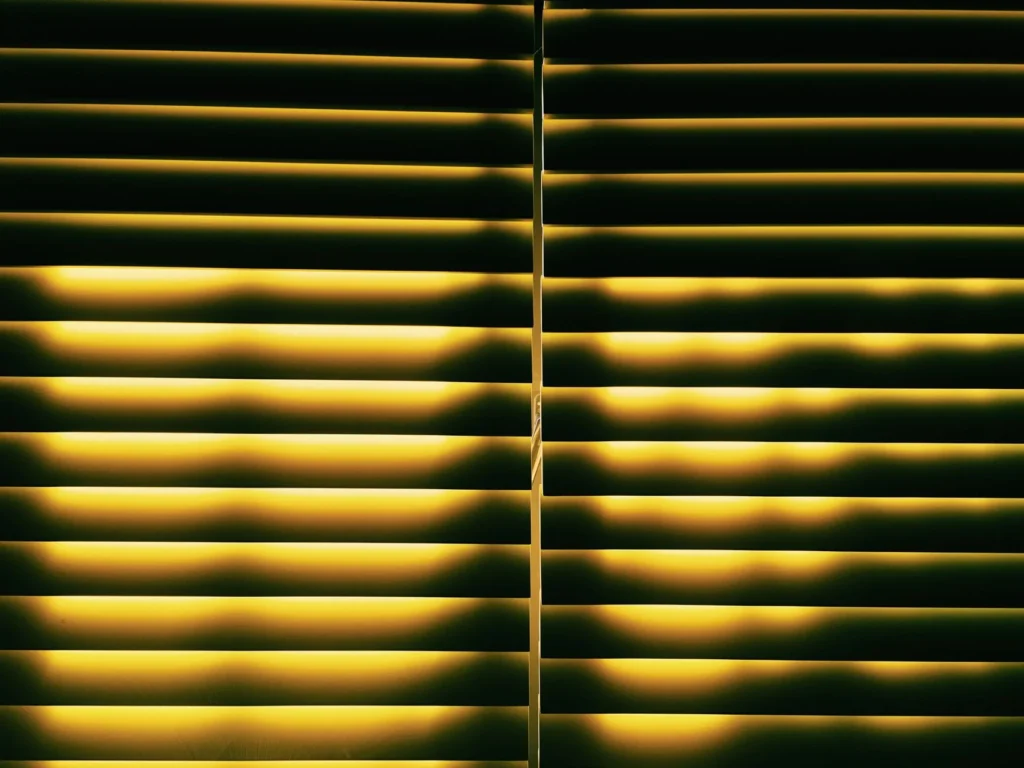 A warm, inviting pattern of light through yellow horizontal blinds creates a cozy indoor atmosphere.
