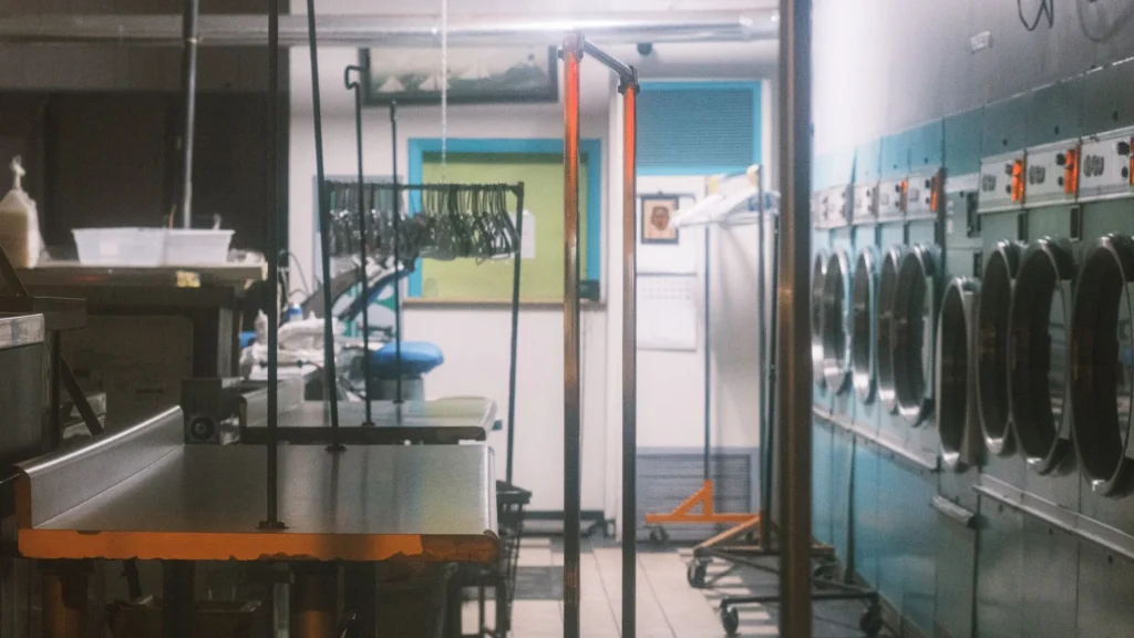 Interior view of a commercial laundry facility with machines and clothing racks.