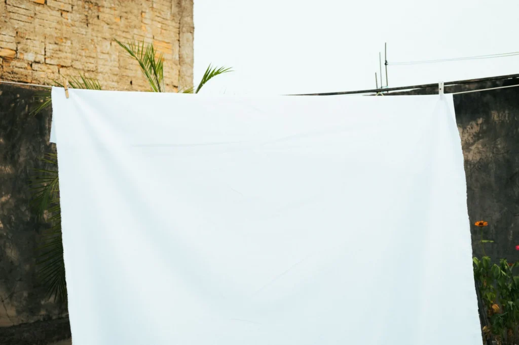A white sheet hangs on a line against a rustic brick wall in a Brazilian backyard.