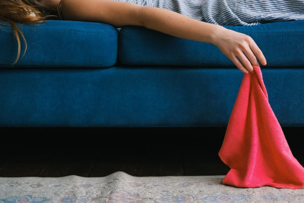 Crop unrecognizable female with dusting cloth in hand lying on sofa while resting after cleaning apartment