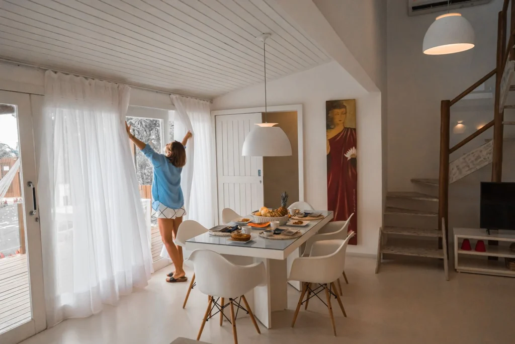 Bright dining room with modern decor and a person opening curtains, creating a warm and inviting atmosphere.