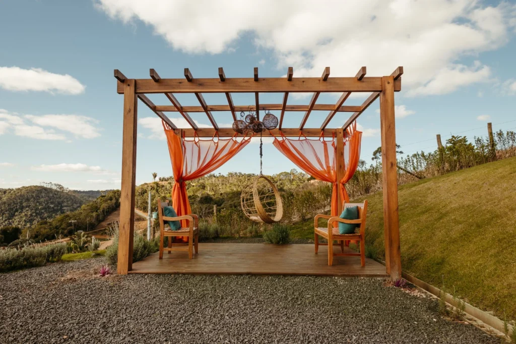 Beautiful rural gazebo with wicker swing and armchairs during summer in countryside setting.