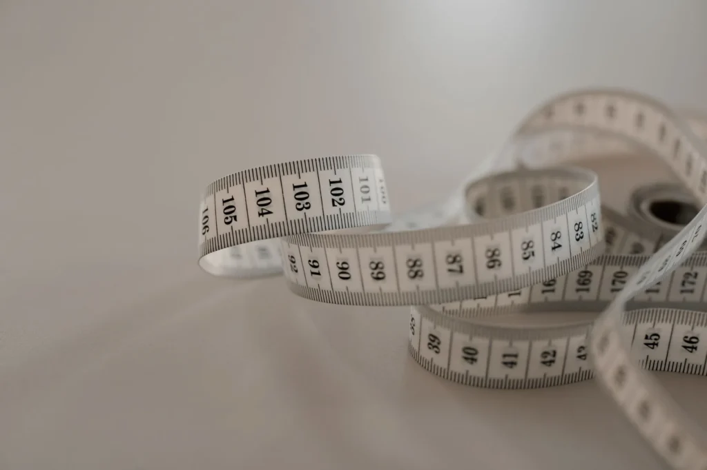 White tape measure with black numbers, coiled loosely on a plain surface.