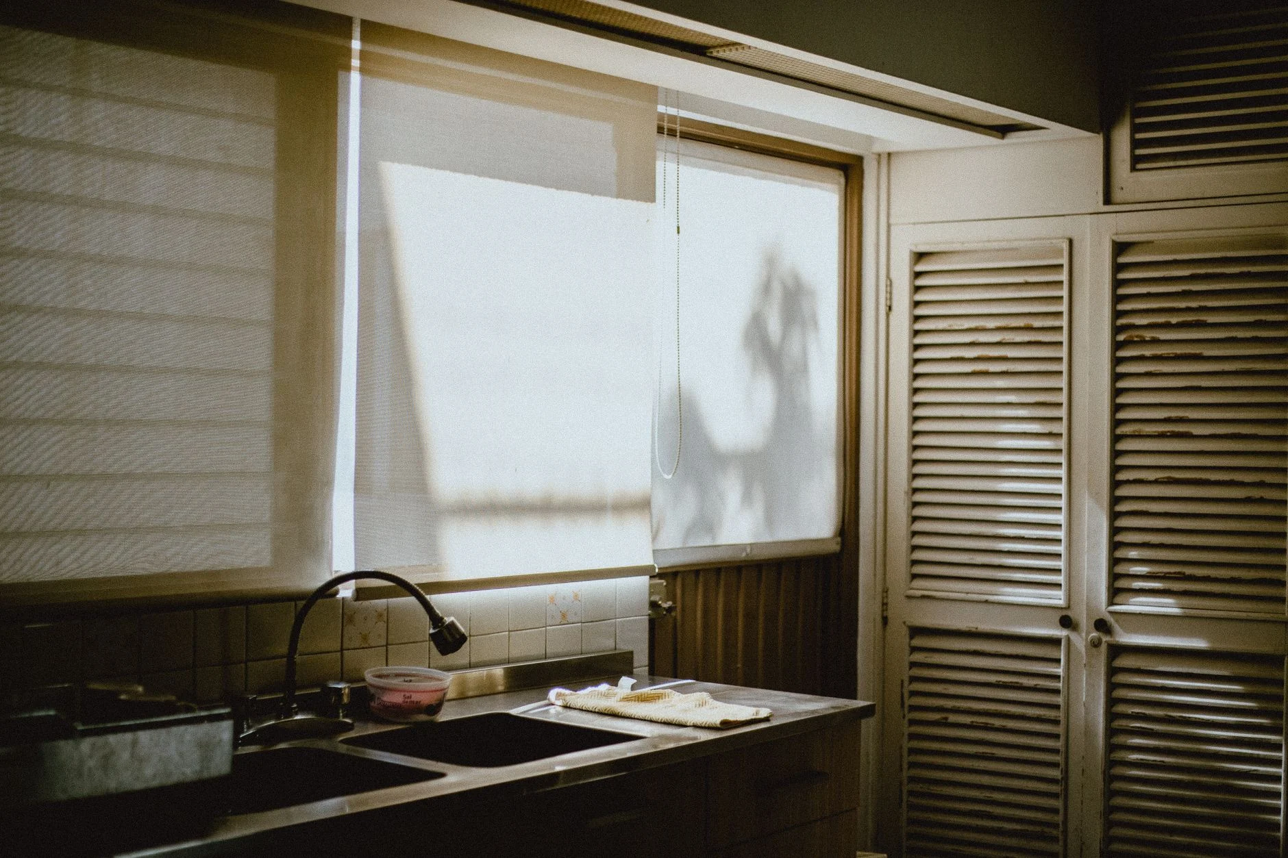 A warm kitchen interior showcasing natural daylight through window blinds and rustic cabinetry.