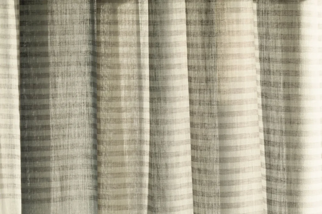 A close-up of transparent striped curtains with sunlight casting interesting shadows.