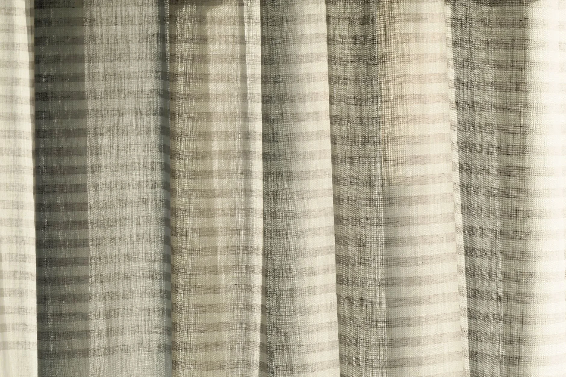 A close-up of transparent striped curtains with sunlight casting interesting shadows.