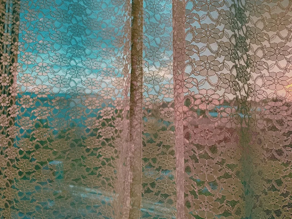 White lace curtain hanging on window with view of modern residential complex houses in early evening
